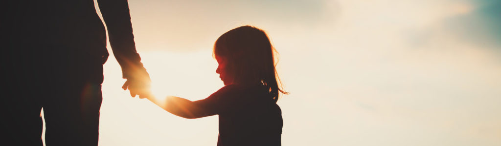 Silhouette de petit enfant tenant la main d’un parent au coucher du soleil
